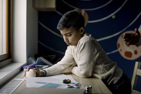 Autistic boy holding stress ball while reading book at home - MASF25576