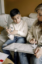 Mutter unterrichtet autistischen Jungen, während er auf dem Sofa im Wohnzimmer sitzt - MASF25594