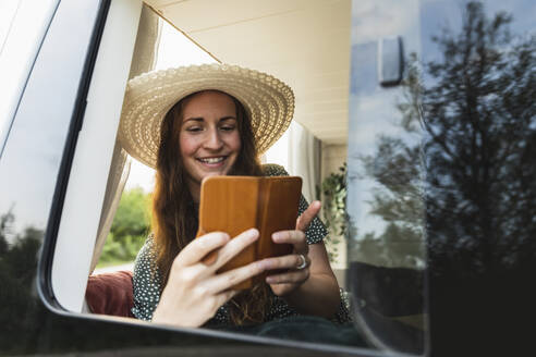 Lächelnde Frau, die ihr Smartphone benutzt, während sie im Wohnmobil sitzt - MASF25652