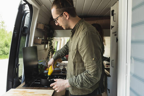 Seitenansicht eines Freundes, der mit seiner Freundin im Wohnmobil Essen zubereitet - MASF25659