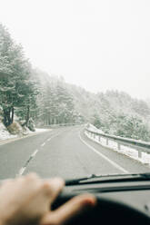 Blick durch die Windschutzscheibe auf einen nicht erkennbaren Reisenden, der einen Transport auf der Straße am Pico Aunamendi in den Pyrenäen an einem Wintertag in Navarra, Spanien, fährt - ADSF29950
