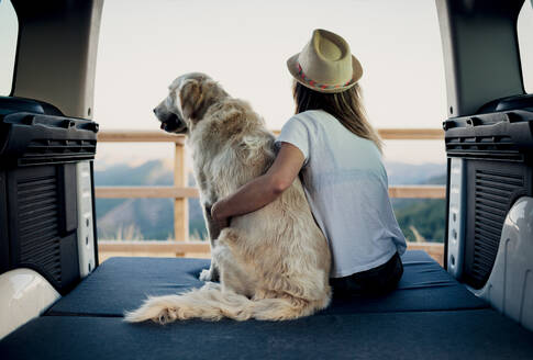 Unbekannte Touristin umarmt gehorsamen Golden Retriever Hund, der auf einer Matratze im Wohnmobil liegt und die Natur bewundert - ADSF29957