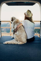 Unbekannte Touristin umarmt gehorsamen Golden Retriever Hund, der auf einer Matratze im Wohnmobil liegt und die Natur bewundert - ADSF29958