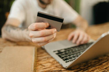 Crop unrecognizable male making purchase with plastic card for order during online shopping via laptop - ADSF29985