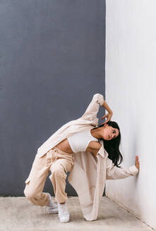 Creative female dancer dancing in city street and leaning on wall during performance - ADSF29999