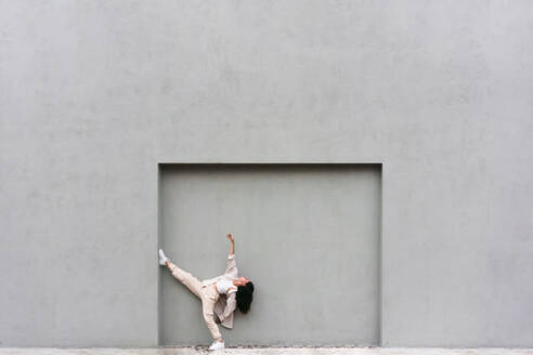 Creative cool female leaning on gray wall and dancing expressively in city street - ADSF30002