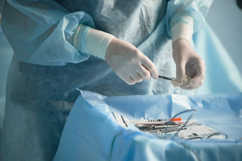 Anonyme OP-Schwester mit Einweghandschuhen desinfiziert die Nadel eines Injektors bei der Vorbereitung auf eine Operation in der Klinik - ADSF30027