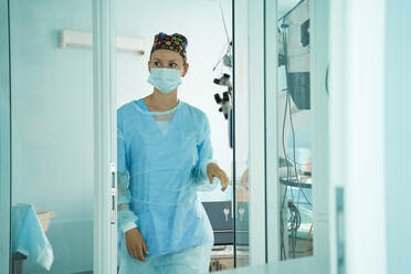 Cheerful adult female medic in sterile mask and ornamental cap looking away in hospital - ADSF30036