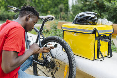 Junger Zusteller, der sein Fahrrad auf der Bank aufpumpt - XLGF02293