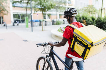 Zusteller benutzt Smartphone, während er mit dem Fahrrad auf dem Gehweg fährt - XLGF02321