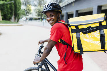Glücklicher junger Zusteller mit Rucksack auf dem Fahrrad sitzend - XLGF02322