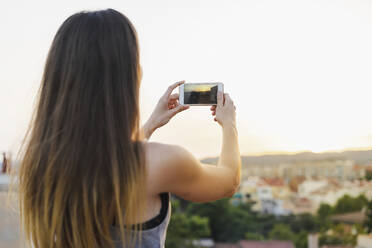 Frau fotografiert Sonnenuntergang Blick durch Smartphone auf dem Dach - AFVF09176