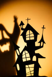 Silhouette eines schwarzen Puppenhauses, das den Schatten eines Geistes auf eine orangefarbene Wand während einer Halloween-Feier wirft - ADSF30066