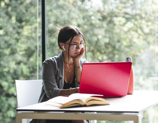 Seitenansicht einer Studentin, die auf einem Netbook tippt, während sie mit einem Buch am Tisch sitzt und Hausaufgaben in der Universitätsbibliothek macht - ADSF30070