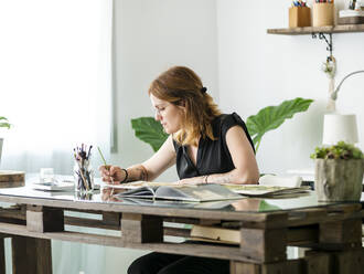 Beschäftigte Designerin malt mit Pinsel auf Papier, während sie an einem Tisch im Kreativbüro sitzt und an einem Projekt arbeitet - ADSF30073