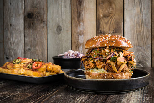 Appetitliche Burger mit gegrilltem Fleisch in der Nähe von Backblech mit Käse Pommes frites mit Paprika und Schüssel mit Salat auf Holztisch im Restaurant platziert - ADSF30077