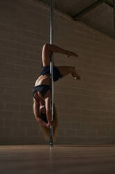 Graceful flexible woman dancing on pole and showing handstand during rehearsal in studio - ADSF30163