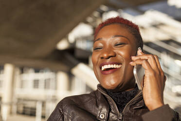 Seitenansicht der schönen schwarzen afro Frau im Gespräch mit ihrem Smartphone beim Lächeln auf Unschärfe Hintergrund an einem sonnigen Tag - ADSF30173