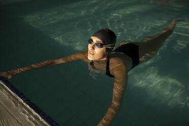 Junge schöne Frau am Rande des Hallenbades, in schwarzem Badeanzug, schwimmt im Wasser - ADSF30181