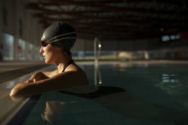 Junge schöne Frau am Rande des Hallenbades, in schwarzem Badeanzug, schwimmt im Wasser - ADSF30182