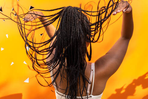 Rückenansicht einer nicht erkennbaren Afroamerikanerin, die lange geflochtene Haare auf lebhaftem gelben Hintergrund in Barcelona wirft - ADSF30188