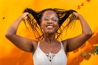 Afroamerikanische Frau wirft langes geflochtenes Haar auf lebhaftem gelben Hintergrund in Barcelona - ADSF30189