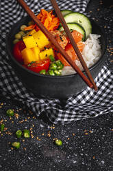 High angle of Asian poke with salmon and rice with assorted vegetables served in bowl on table with chopsticks in restaurant - ADSF30194