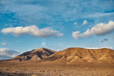 Weiße Wolken schweben am strahlend blauen Himmel über einem trockenen Tal und Hügeln an einem Sommertag in Fuerteventura, Spanien - ADSF30198