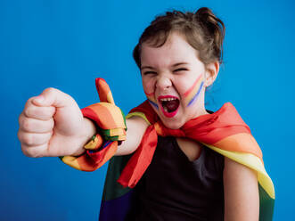 Cute glad child with multicolored bandage on neck and wrist standing against blue background and looking at camera - ADSF30213