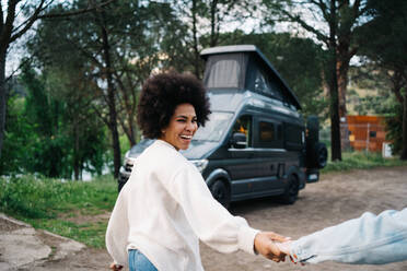 Lächelnde afroamerikanische Frau, die die Hände ihres beschnittenen Freundes hält, während sie spazieren geht und gegen das Wohnmobil schaut - ADSF30227