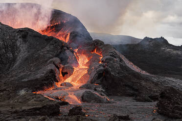 Malerische Ansicht des Fagradalsfjall mit schnellem Feuer und Lava unter diffusem Rauch in Bergen mit Wolken in Island - ADSF30233