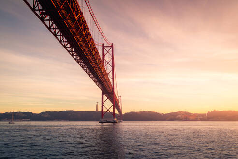 Von unten rostige Metallmasten am Ufer des Tejo unter der Brücke 25 de Abril bei Sonnenuntergang in Lissabon, Portugal - ADSF30236