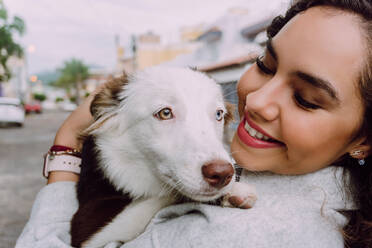 Entzückte Besitzerin umarmt süßen Border Collie Hund und lächelt mit geschlossenen Augen - ADSF30237
