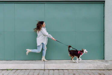 Side view of female owner running with Border Collie dog on leash while having fun during stroll in city - ADSF30239