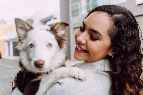 Entzückte Besitzerin umarmt süßen Border Collie Hund und lächelt mit geschlossenen Augen - ADSF30241