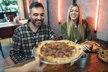 Frau bietet männlichen und weiblichen Freunden im Restaurant eine Pizza an - JSRF01579