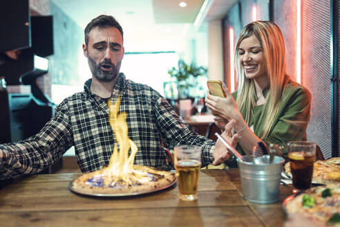 Glückliche Frau fotografiert Pizza von männlichem Freund, der im Restaurant schreit - JSRF01582