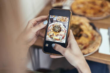 Mid adult woman photographing pizza through smart phone in restaurant - JSRF01587