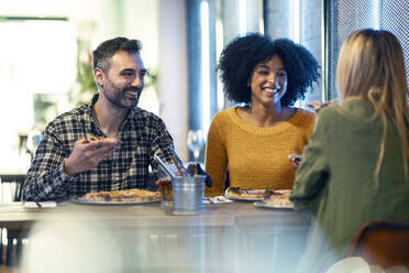 Happy male and female friends enjoying pizza in restaurant - JSRF01588