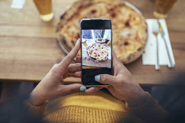 Young woman photographing pizza through smart phone - JSRF01589