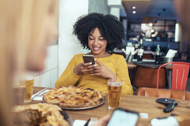 Afro-Frau, die ein Mobiltelefon benutzt, während sie mit einer Freundin im Restaurant sitzt - JSRF01599