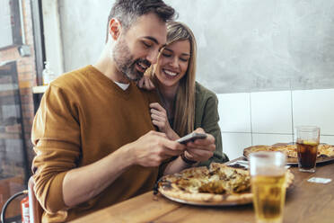 Bearded man sharing mobile phone with female friend at table - JSRF01603