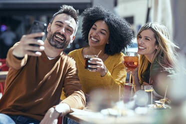 Fröhlicher Mann macht Selfie mit Freundinnen im Restaurant - JSRF01612