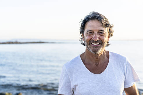 Mature man smiling while standing at beach - DLTSF02152