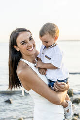 Glückliche Frau mit Sohn am Strand bei Sonnenuntergang - DLTSF02155