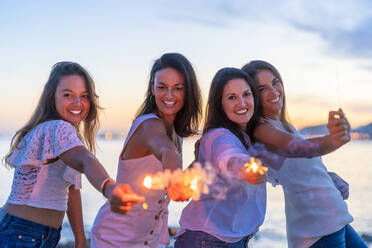 Fröhliche Freundinnen haben Spaß mit Wunderkerzen am Strand bei Sonnenuntergang - DLTSF02163