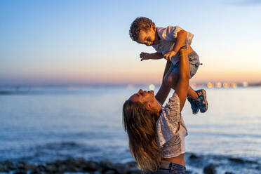 Cheerful mother lifting son at beach - DLTSF02166