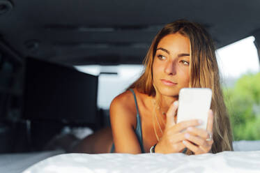 Frau mit Smartphone entspannt sich im Wohnmobil im Urlaub - PGF00798