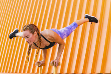 Rothaarige Sportlerin im Handstand vor einer orangen Wand - MGRF00432