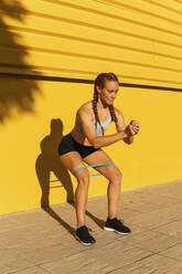 Sportlerin, die mit einem Widerstandsband vor einer gelben Wand trainiert - MGRF00437